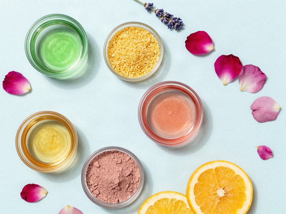 Botanical extract, beeswax, rose and pink clays in open glass dishes with rose petals, lavender and citrus.