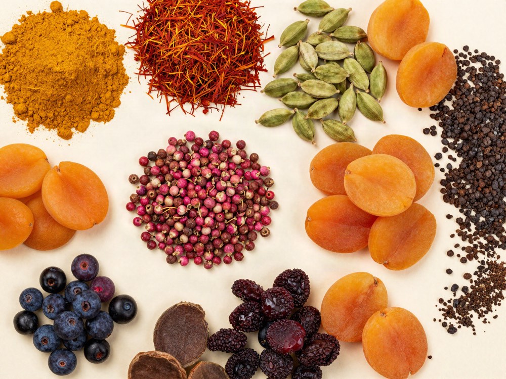 Turmeric, saffron, cardamom, pink peppercorns, dried apricots and berries laid out on a pale surface.