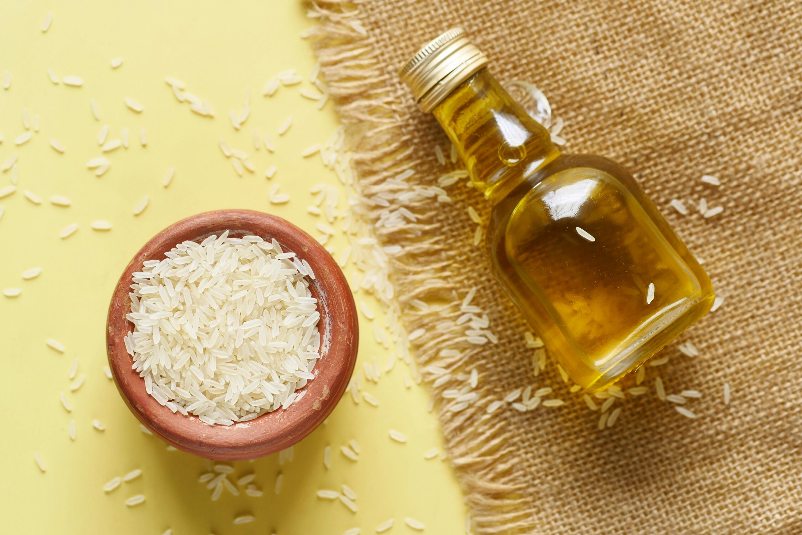 Home Close-up of rice in a ceramic bowl with a bottle of oil on a burlap background.